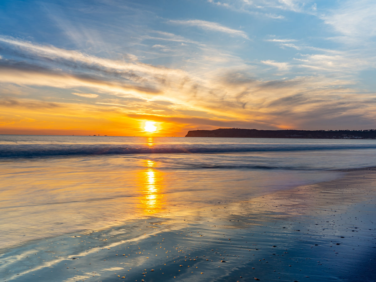 Golden ocean sunset at Coronado Beach with waves reflecting the bright orange sky and Point Loma visible in the distance