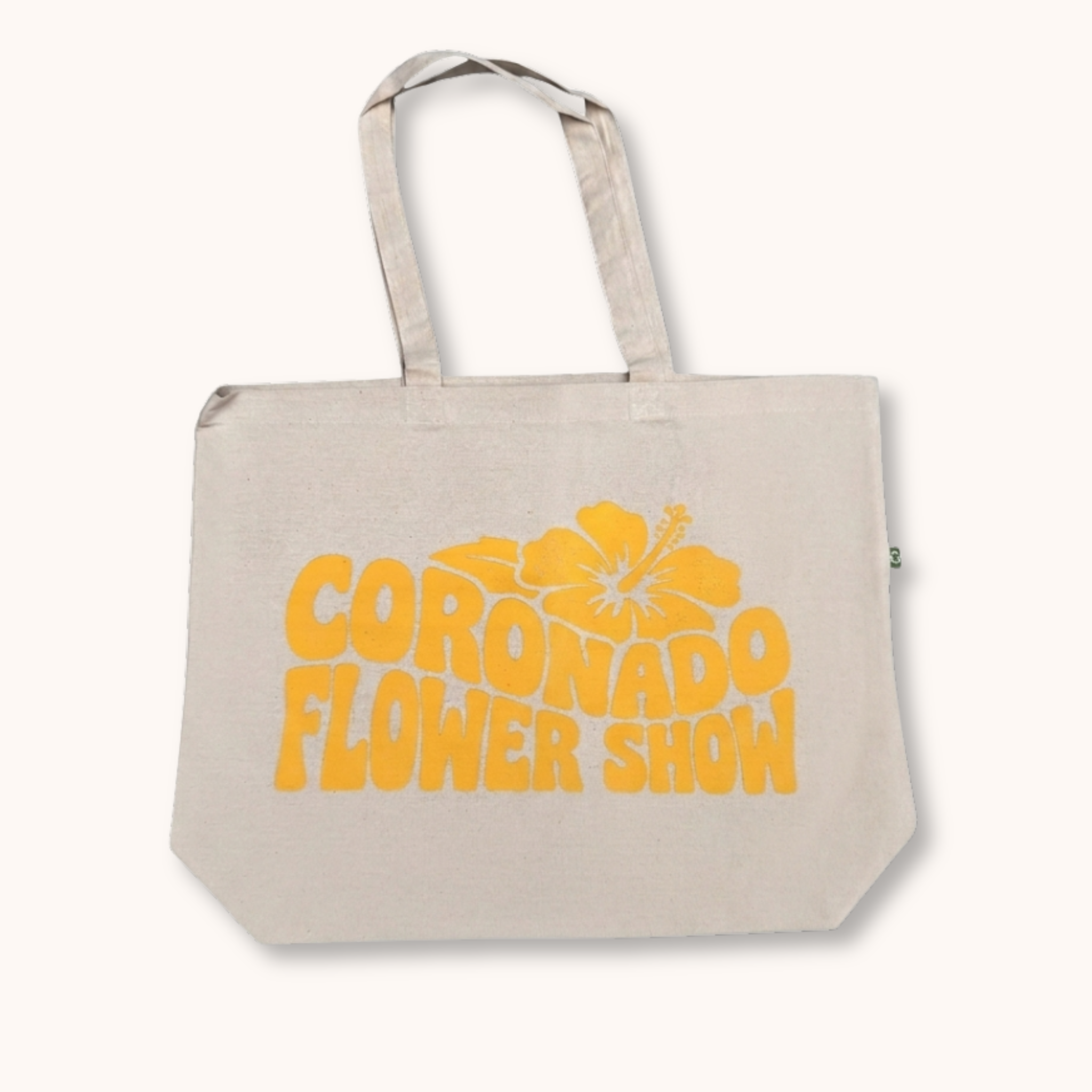 Beige tote bag with 'Coronado Flower Show' text and yellow flower graphic on a white background