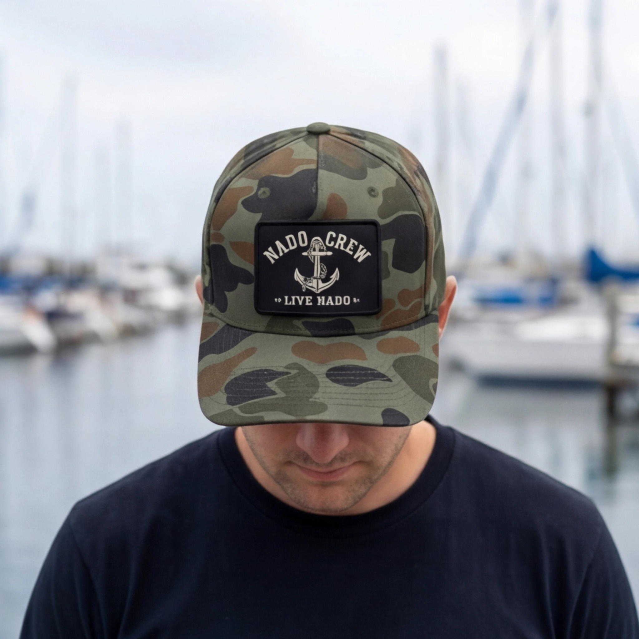 Person wearing a camouflage cap with a logo in front of a marina