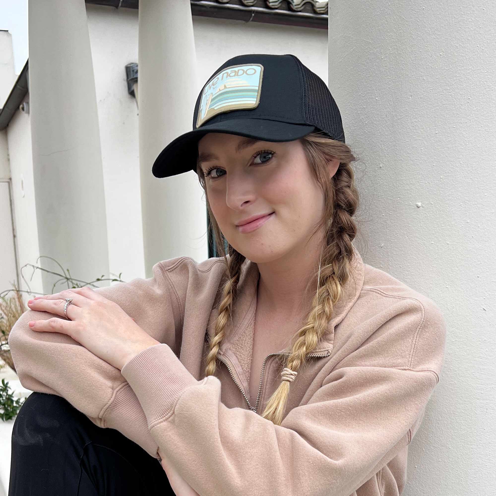 woman wearing black curved bill trucker with neutral greens embroidered surfboard patch from live nado coronado california