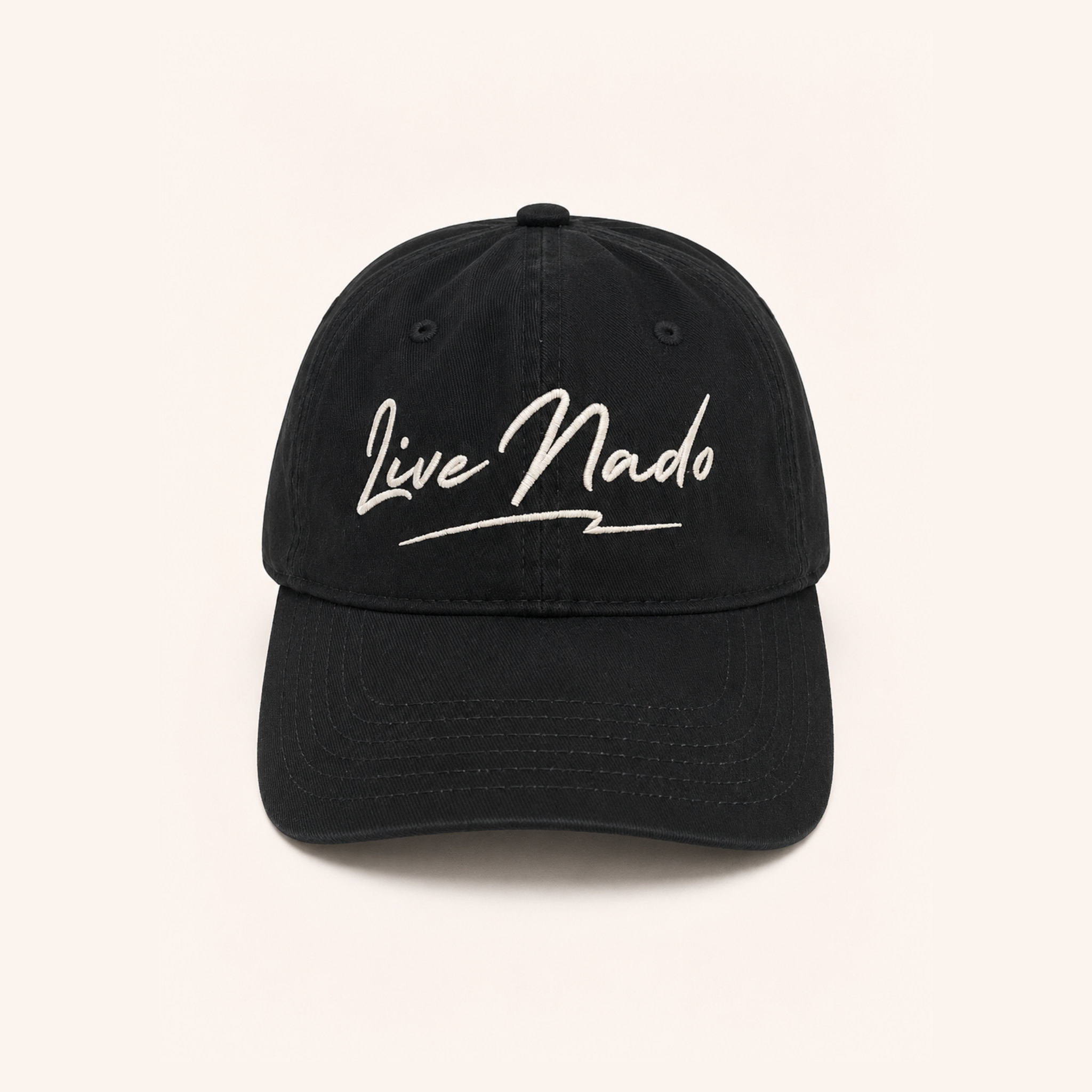 Front-facing view of a washed black cotton baseball cap centered against an off-white background. The crown features cream-colored embroidered cursive text reading "Live Nado" with a stylized underline.