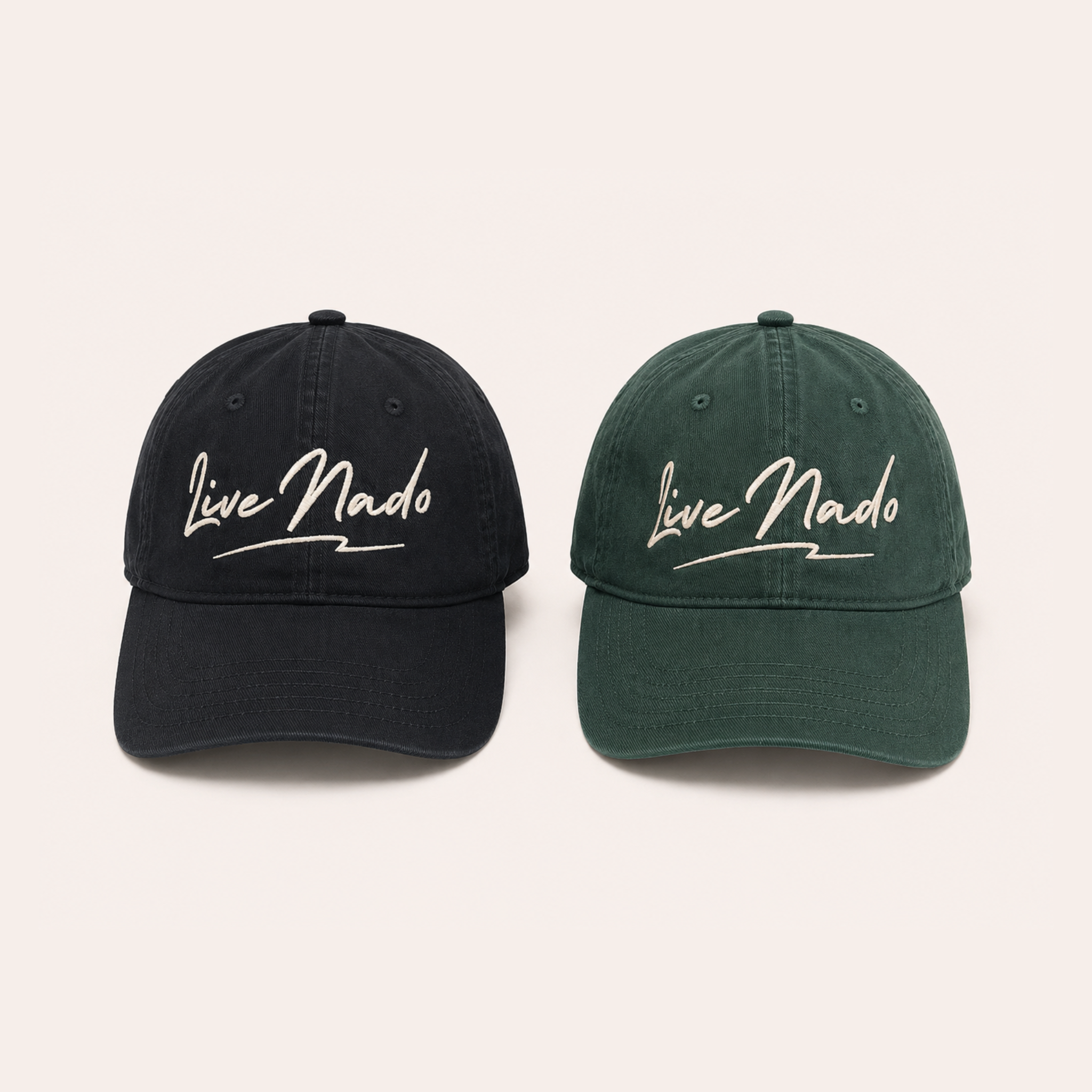 Front-facing view of two relaxed baseball caps placed side by side against a plain off-white background. The hat on the left is washed black, and the hat on the right is washed dark green. Both feature cream-colored embroidered cursive text reading "Live Nado" with an underline.
