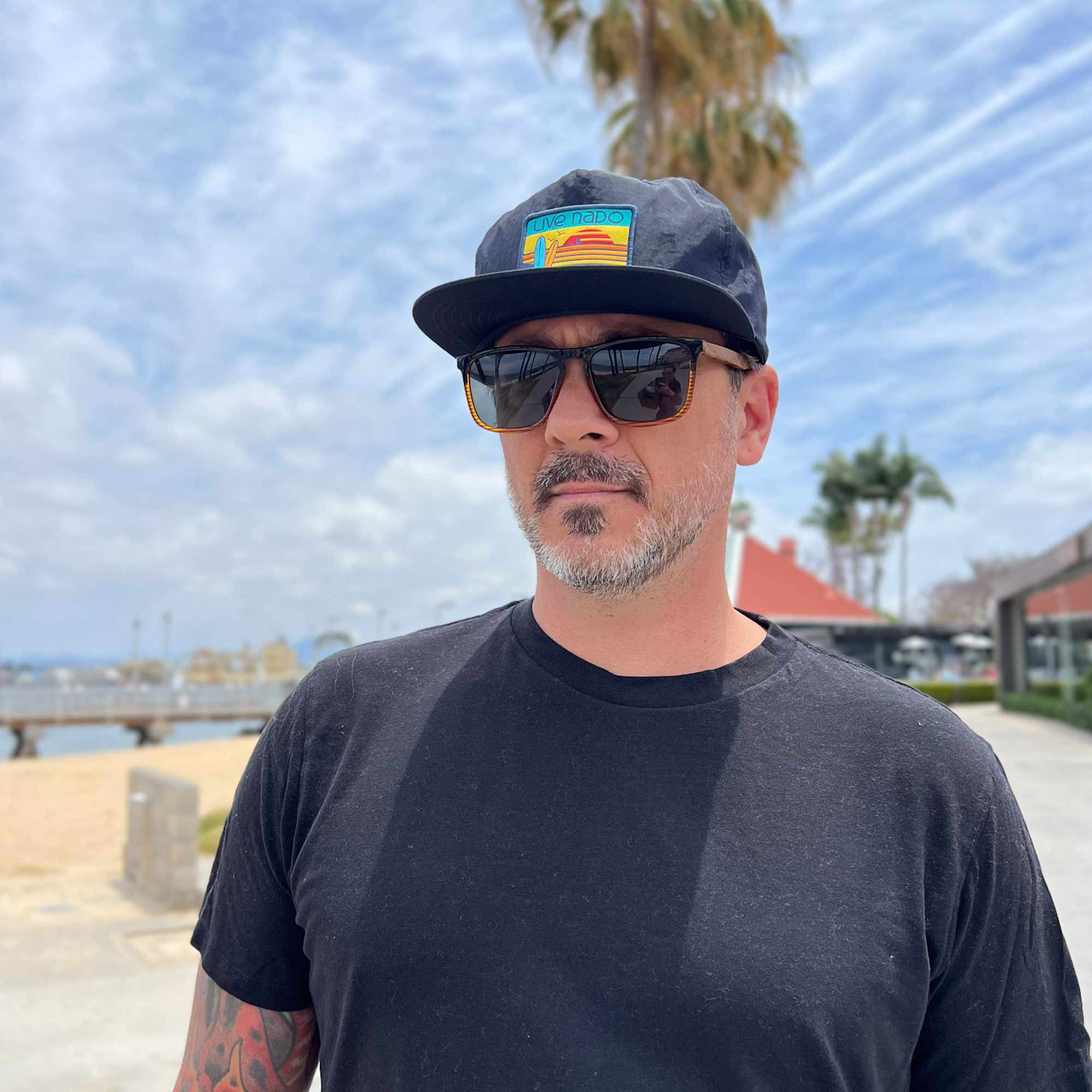man in navy flat brim surf cap with retro colored embroidered surf board patch stand by the Coronado Ferry Landing