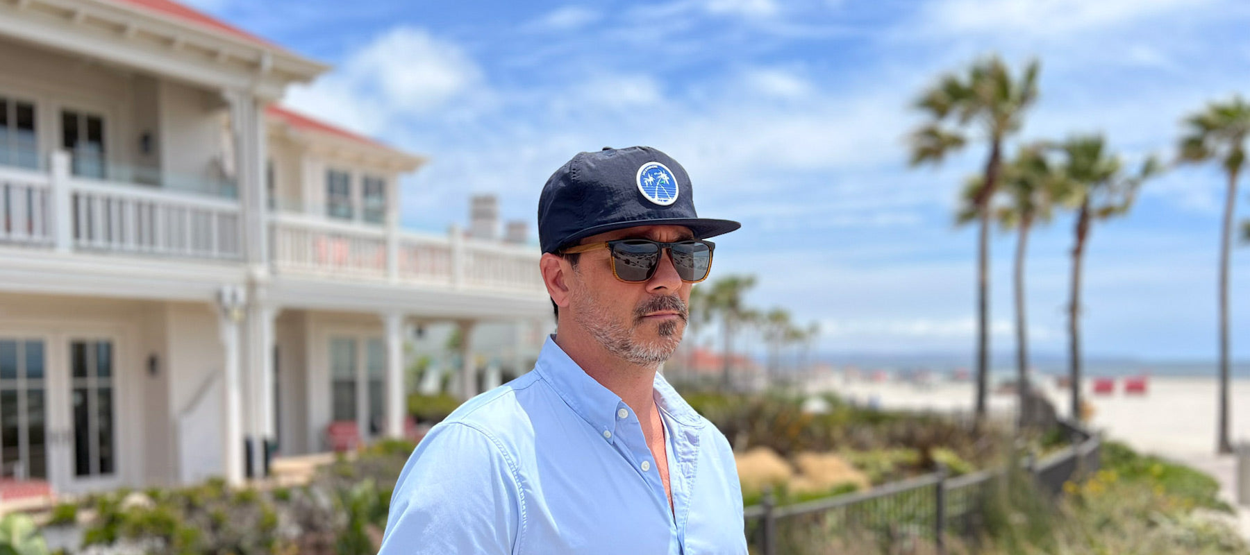 Man standing at the Hotel Del Coronado, wearing navy colored flat brim, water resistant, quick dry surf cap,