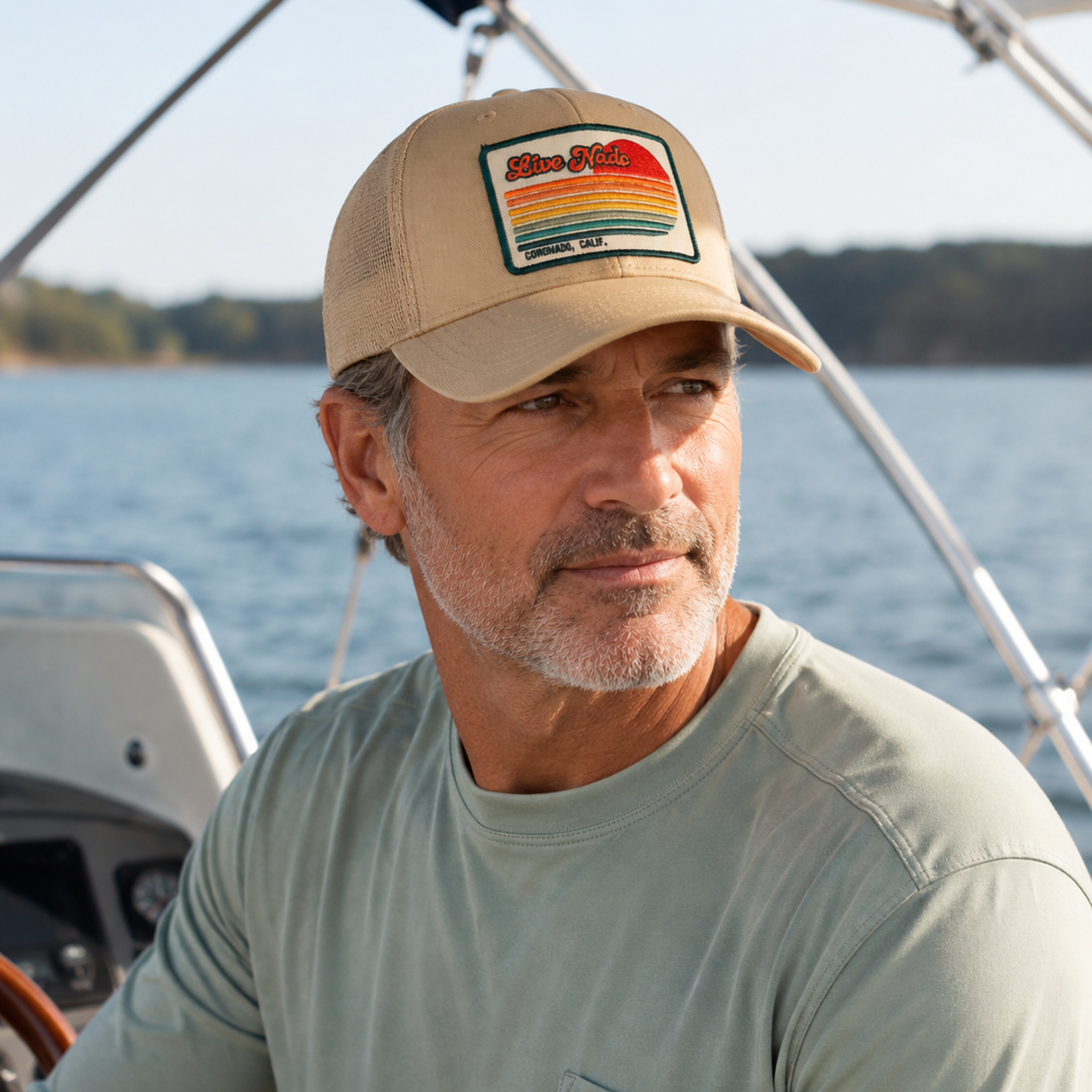 Man wearing a cap with a patch on a boat by a body of water
