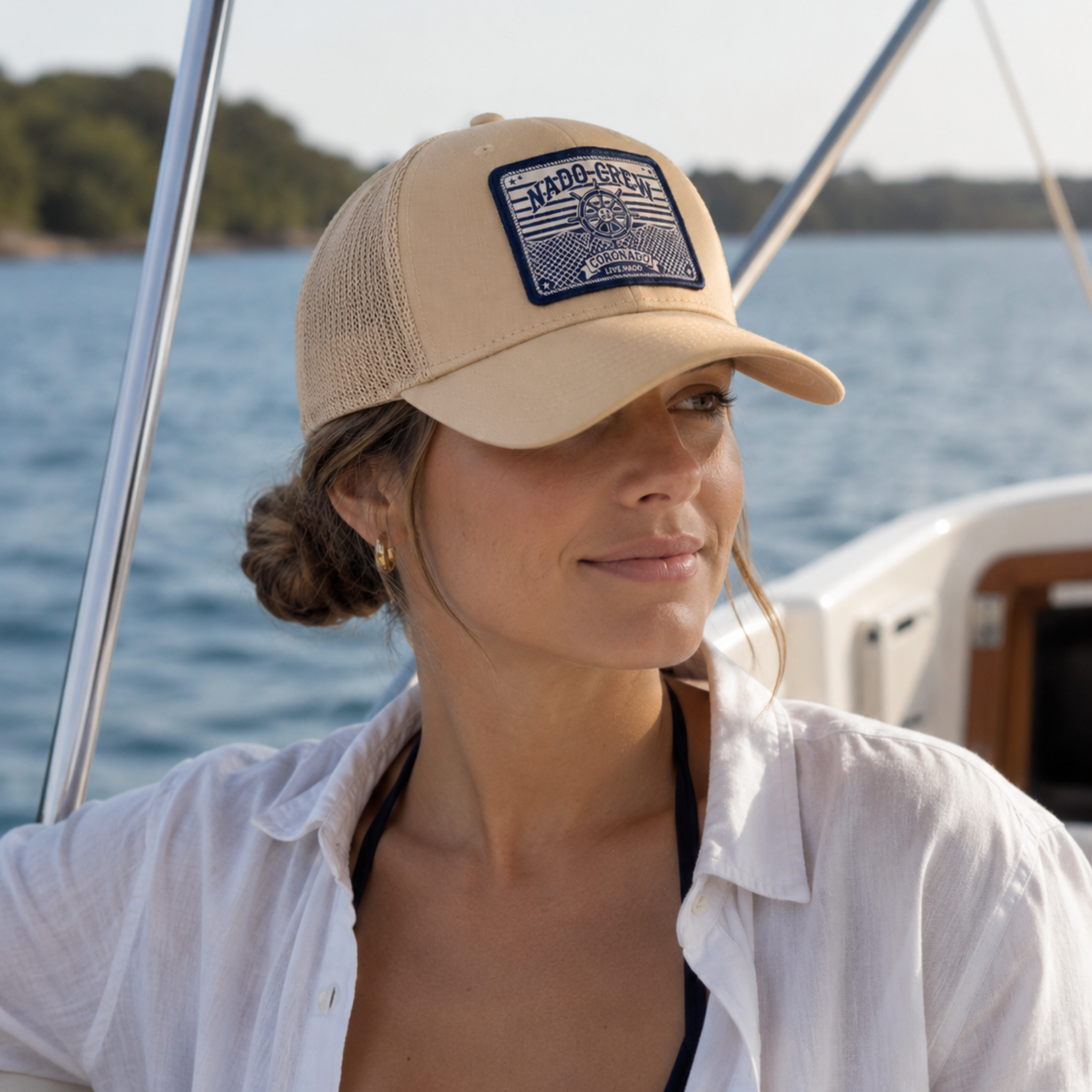 Woman wearing a beige cap with a logo on a boat, surrounded by water and trees.