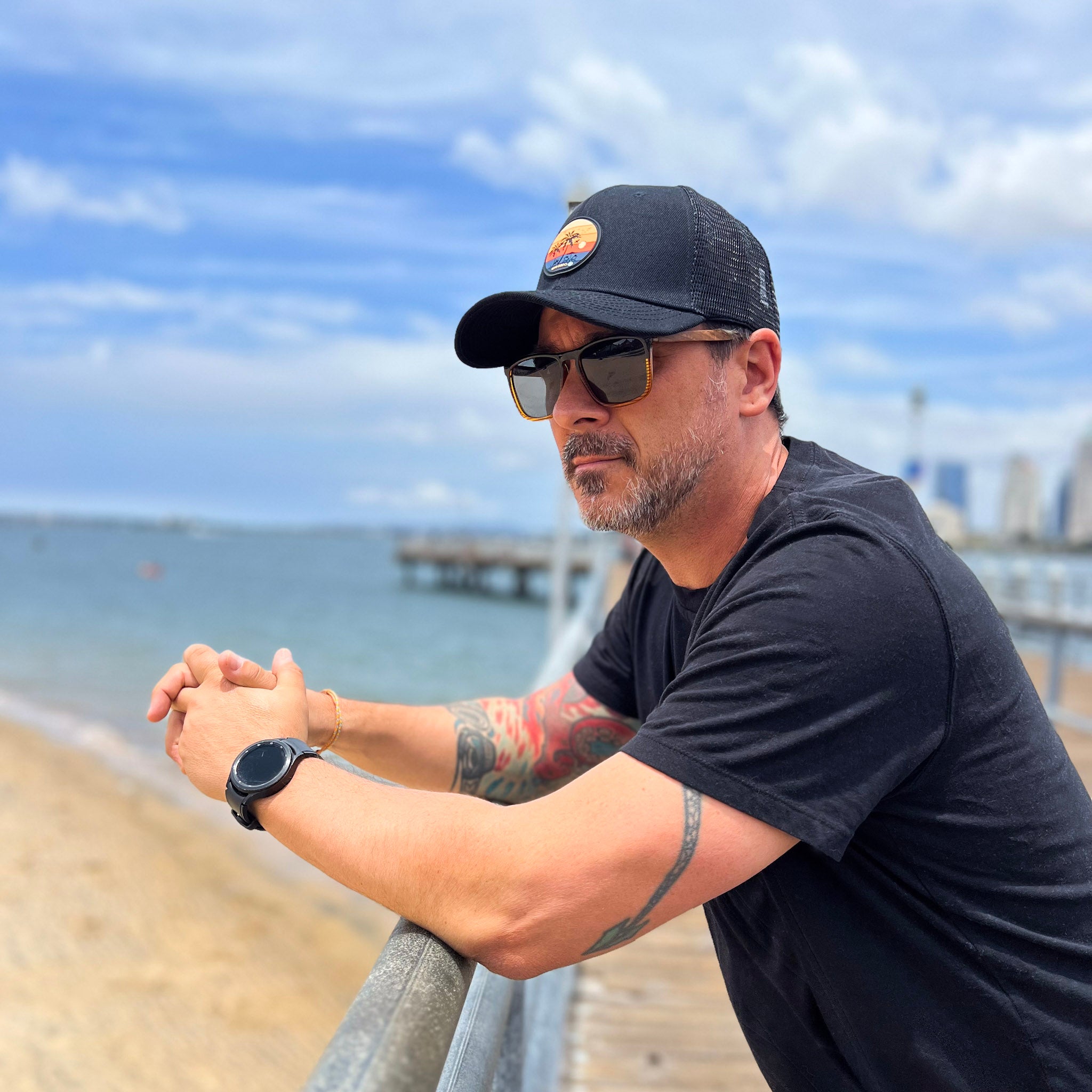 guy wearing black curved bill snapback trucker with a sunset silicone patch standing at the ferry landing in coronado