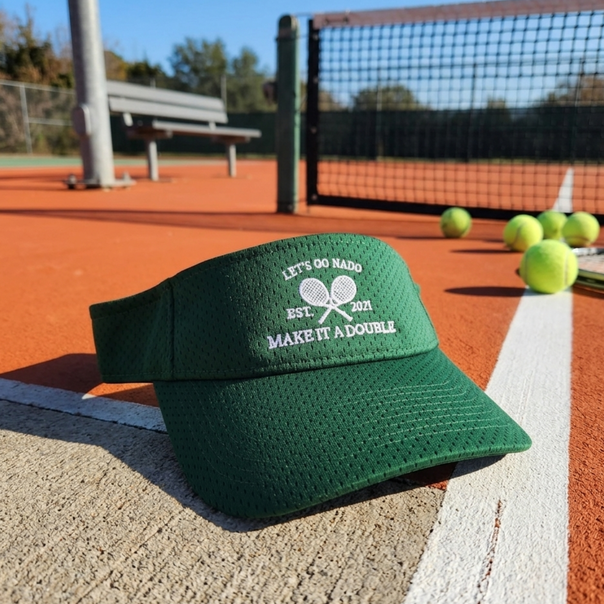 Green visor with text on a tennis court with tennis balls