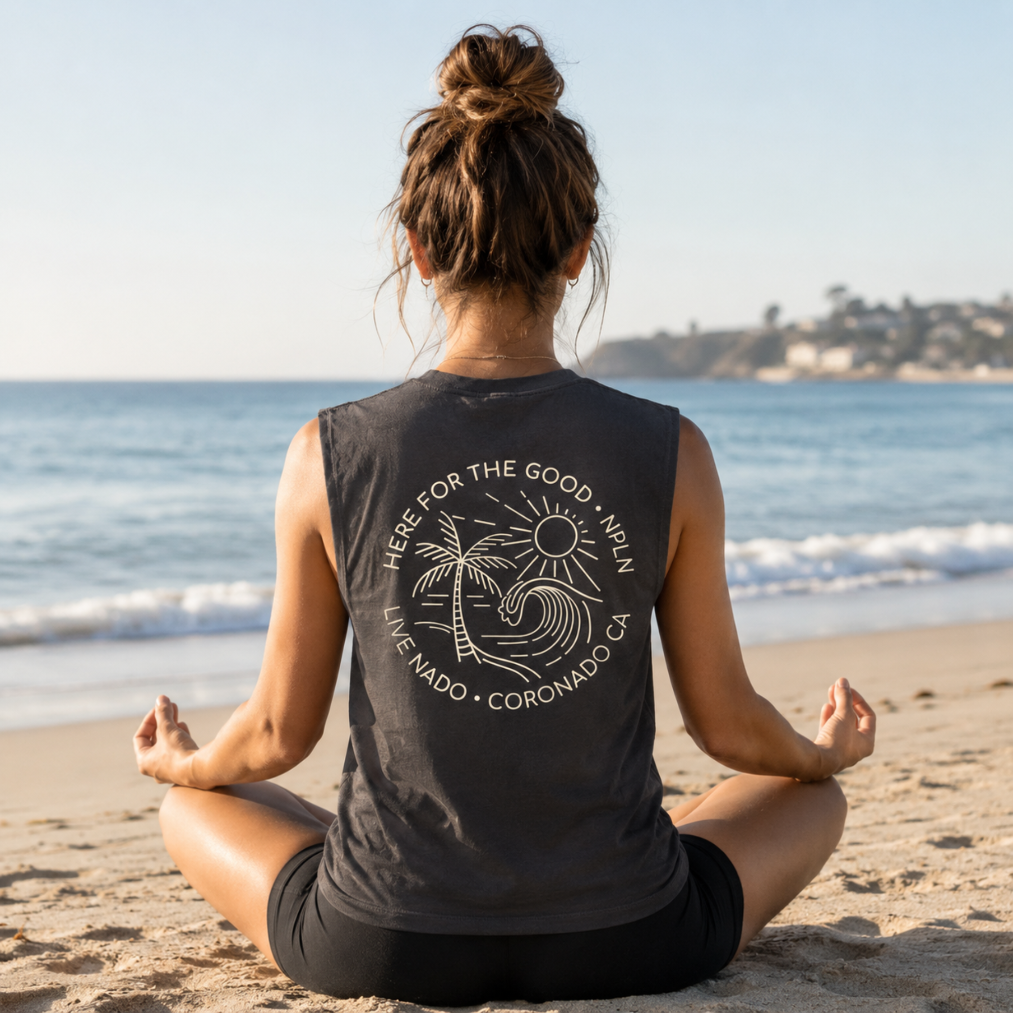 Person meditating on a beach wearing a sleeveless shirt with a logo.