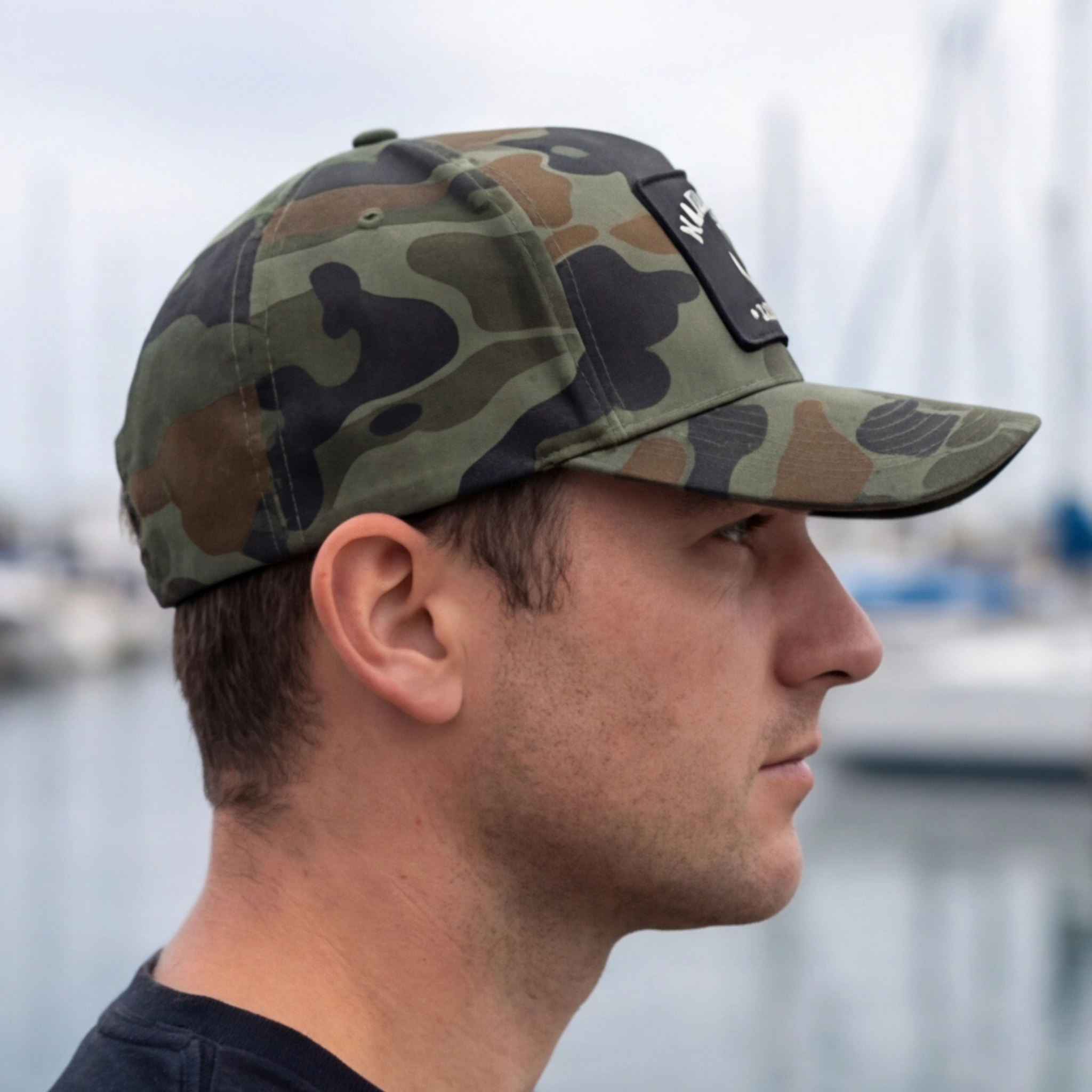Man wearing a camouflage cap with a blurred background of water and boats