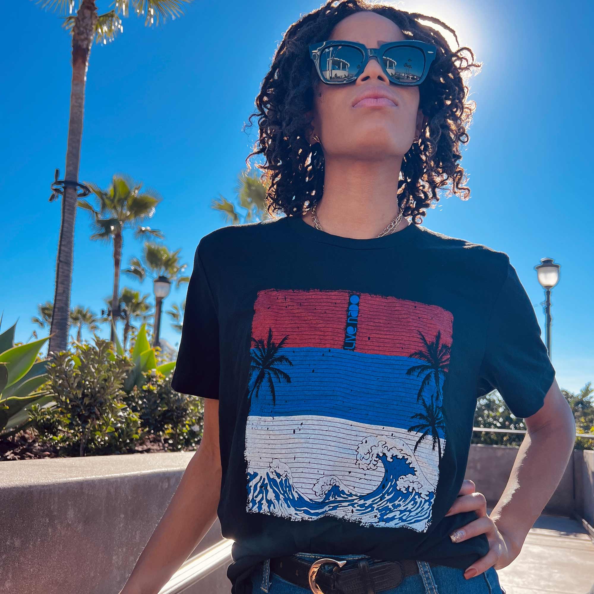 beachy and patriotic woma wearing black tshirt with red white and blue waves and sky with palm tree design