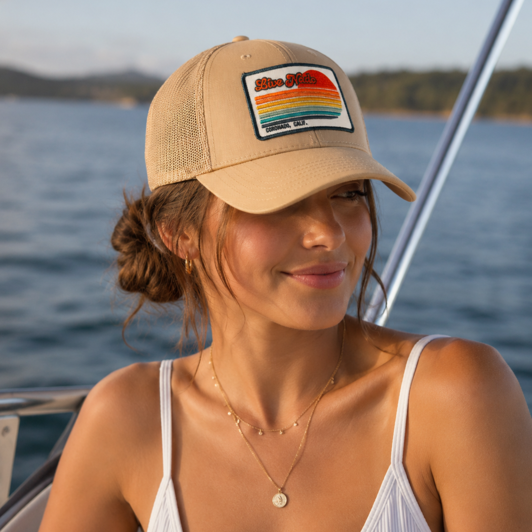 Woman wearing a beige cap with a colorful patch on a boat, water and sky in the background