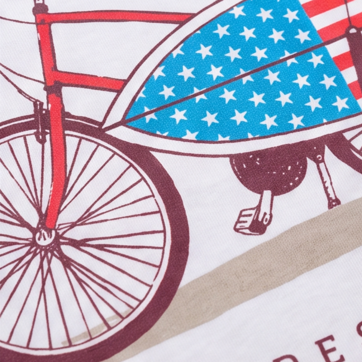 Macro close-up of a t-shirt graphic showing the front wheel of a red bicycle and an American flag-patterned surfboard.
