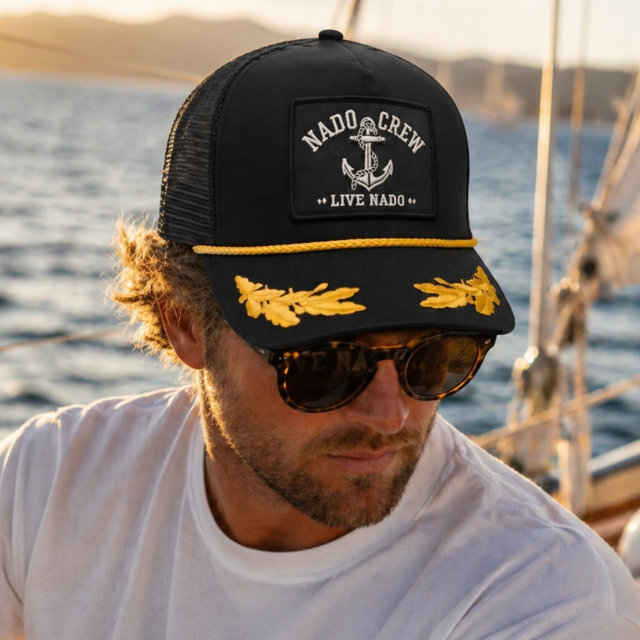 Man wearing a black cap with 'Nado Crew' logo and sunglasses, on a boat with water in the background
